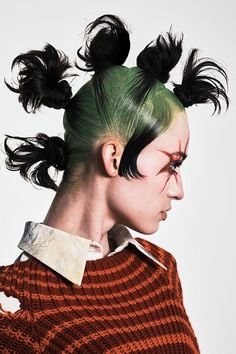 a woman with green hair and black mohawks on her head, wearing an orange sweater