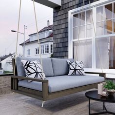 a porch swing with pillows on it next to a window