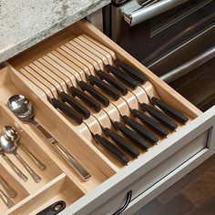 an open drawer with utensils and spoons in it on a kitchen counter