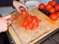 a person cutting up tomatoes on top of a wooden cutting board