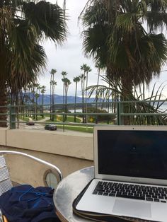 an open laptop computer sitting on top of a metal table next to a palm tree