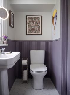 a white toilet sitting next to a sink in a bathroom under a painting on the wall