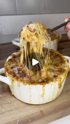 a person holding a spoon full of food in a casserole dish on a cutting board