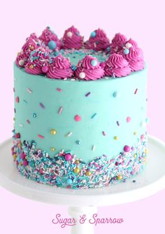 a blue cake with pink frosting and sprinkles on top is sitting on a white plate