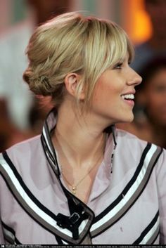 a woman with blonde hair wearing a white shirt and black tie smiling at someone in the background