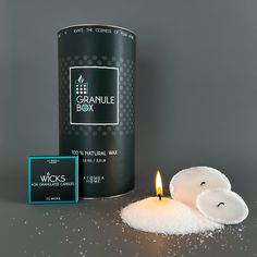 a candle next to a can of granule box on a grey surface with sparkles around it