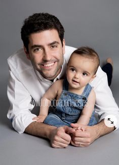 a man holding a baby in his arms and smiling at the camera while laying on the floor