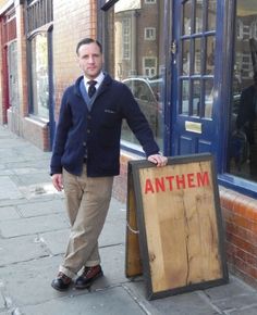 a man standing next to a wooden sign on the side of a street in front of a building