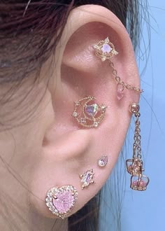 a woman wearing ear piercings with pink stones and chains on her ears, behind the ear