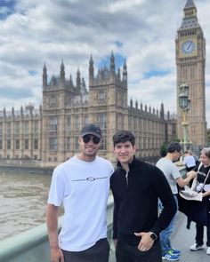 two men standing next to each other in front of the big ben clock tower