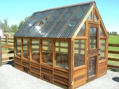 a small wooden building sitting on top of a gravel lot next to a fence and grass field