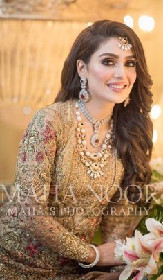 a woman in a bridal outfit sitting next to flowers and smiling at the camera