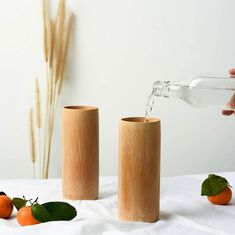 someone is pouring water into two wooden vases with oranges on the table next to them