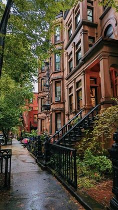 an alleyway with many brownstone buildings and trees on both sides in the rain