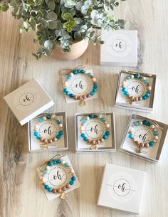 six personalized bracelets in boxes on a wooden table with flowers and greenery