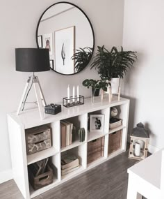 a white bookcase with books and plants on it in front of a round mirror