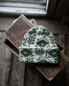 a green and white knitted hat sitting on top of a piece of wood next to a window