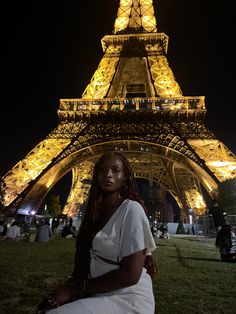 a woman sitting in front of the eiffel tower at night with her hands on her hips