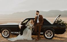 a man and woman standing next to a black car