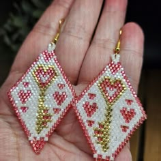 a pair of red and white beaded earrings in the palm of someone's hand