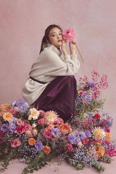 a woman sitting on top of a pile of flowers holding a flower in her hand