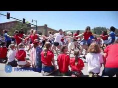 a group of people in red shirts and blue shorts are sitting on the sidewalk with their arms around each other