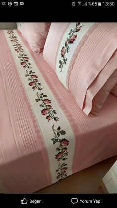 a bed covered in pink sheets and pillows with embroidered flowers on the bottom, along with matching pillow cases