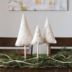 three knitted christmas trees sitting on top of a table next to a wooden bench