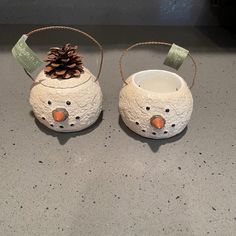 two snowmen made out of clay sitting on top of a counter next to a pine cone