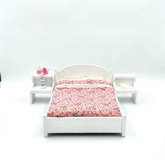 a dollhouse bed with pink bedspread and nightstands next to it on a white background