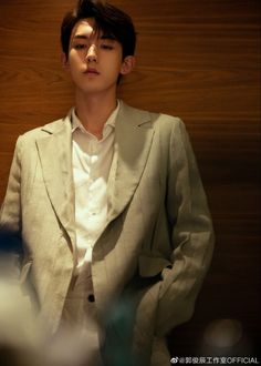 a young man in a suit standing next to a wooden wall