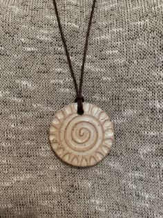 a white necklace with a spiral design on the front and brown cord attached to it