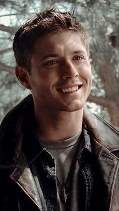 a young man smiling at the camera with trees in the background behind him