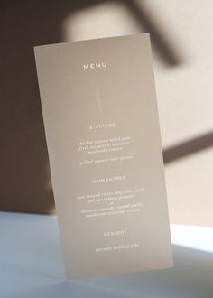 the menu card is sitting on top of a white table cloth, with a shadow cast on it