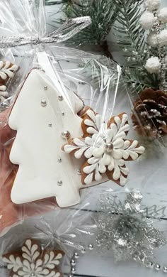 a hand holding a white and brown christmas tree shaped cookie in front of some pine cones