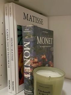 a candle sits next to two books on a shelf