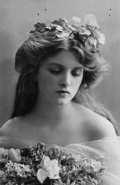 an old black and white photo of a woman with flowers in her hair, wearing a dress