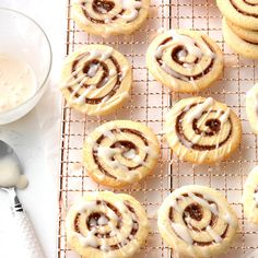 several cinnamon rolls on a cooling rack next to a glass of milk and spoons