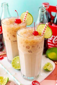 two glasses filled with ice cream and topped with cherries next to bottles of coke