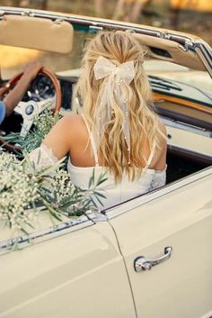 a woman sitting in the driver's seat of a white car with a bow on her head