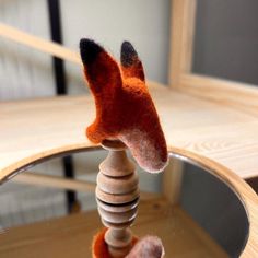 a small stuffed animal on top of a wooden table next to a mirror with its reflection in it