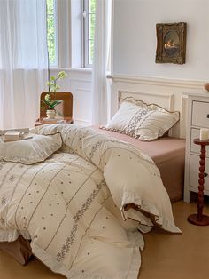 a bed with white comforter and pillows in a bedroom next to a window,