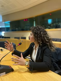 a woman sitting at a table in front of a microphone with her hands out to the side