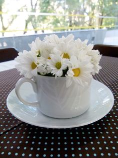 a white cup with some daisies in it on a table next to a window