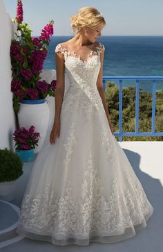 a woman in a wedding dress standing on a balcony next to the ocean and flowers