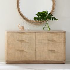 a dresser with a plant on top and a round mirror above it