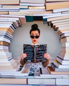 a woman is holding up a book in front of her face while surrounded by stacks of books