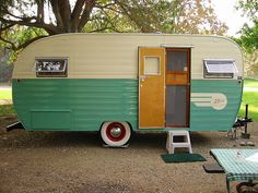 an old camper trailer is parked in the middle of a park with tables and chairs around it