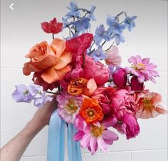 a person holding a bouquet of flowers in front of a white wall with blue ribbon