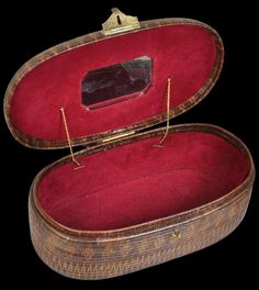 an open wooden box with red velvet lining and gold trimmings on the lid